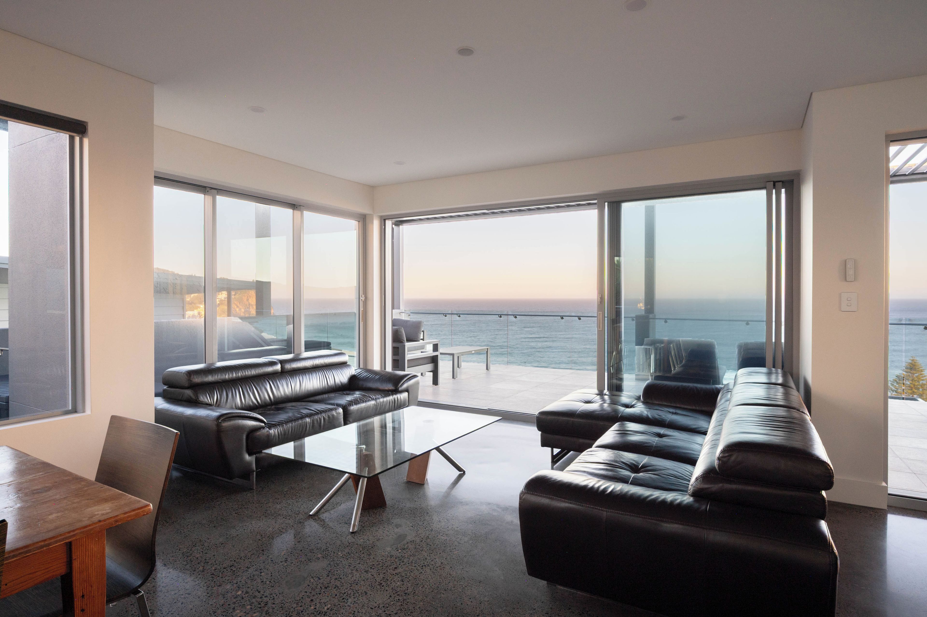 A modern living room with a large glass door leading to a balcony overlooking the sea.