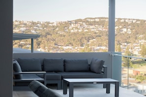 A balcony with a sofa and a table, overlooking a residential area with houses and greenery.