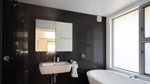 A modern bathroom with a freestanding bathtub, a sink with a mirror above it, and a window providing natural light. - “Oceanview & Seabreeze” - with Pool (Copacabana)