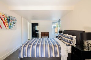 Une chambre à coucher avec un lit, une table de chevet, une commode, une fenêtre et un tableau accroché au mur.