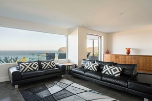 A modern living room with two black leather sofas, a wooden cabinet, and a large window offering a view of the ocean. - “Oceanview & Seabreeze” - with Pool (Copacabana)