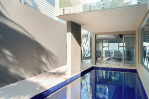 A modern pool area with clear blue tiles, a glass enclosure, and a view of the outdoors.
