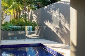 Une piscine à l’eau d’un bleu cristallin, entourée d’un petit muret et d’une végétation luxuriante.