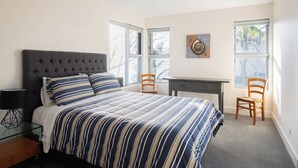 A bedroom with a tufted headboard bed, striped bedding, a desk, two chairs, and a wall clock. - “Oceanview & Seabreeze” - with Pool (Copacabana)