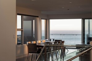 Un comedor moderno con vistas al mar, con barandilla de cristal y mobiliario contemporáneo.
