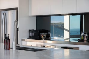 A modern kitchen with a stainless steel refrigerator, a coffee maker, and a view of the ocean.