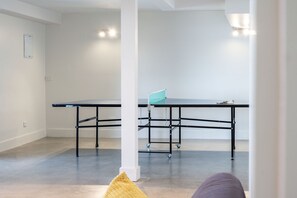 Une pièce moderne et minimaliste, avec une table de ping-pong, un pilier blanc et un luminaire au plafond.