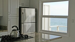 Une cuisine avec des meubles blancs, un réfrigérateur en acier inoxydable, une cuisinière à gaz et une fenêtre donnant sur la mer.