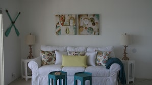 Un canapé blanc agrémenté de coussins colorés, deux petites tables d’appoint de couleur turquoise et un mur orné d’œuvres d’art abstraites.