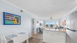 A modern kitchen with white cabinetry, a dining area with a table and chairs, and a view of the ocean through large windows.