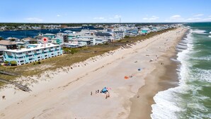 A coastal town with a long sandy beach, a marina with boats, and colorful buildings along the shore.