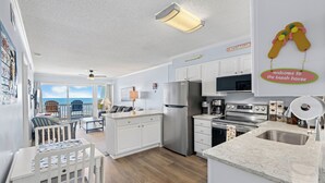 A spacious kitchen with a large island, a refrigerator, and a microwave. There is a view of the ocean through the windows.