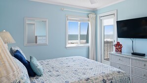 A bedroom with a bed, a dresser, a television, and a window with a view of the beach.