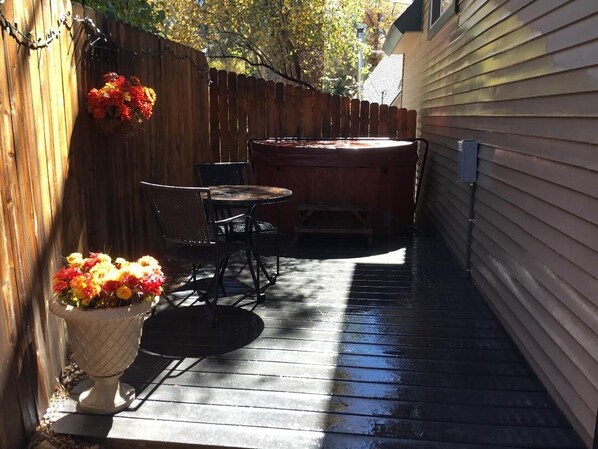 A wooden deck with a hot tub, a table, and chairs.