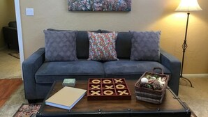 Ein Wohnzimmer mit Sofa, Couchtisch, einem Gesellschaftsspiel, einer Lampe und einem Gemälde an der Wand.