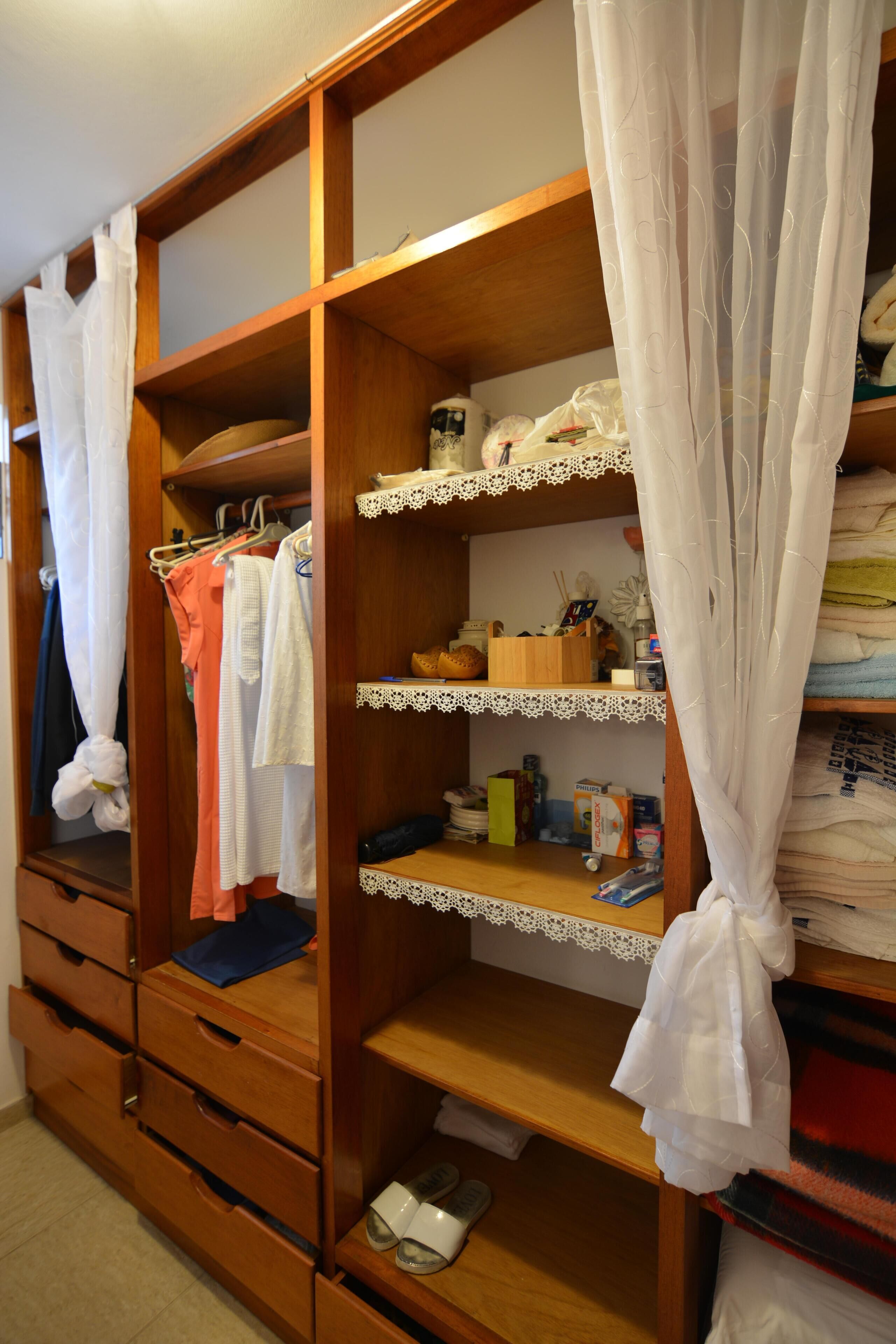 A wooden wardrobe with multiple shelves and drawers, a hanging rack, and a pair of shoes on the bottom shelf.