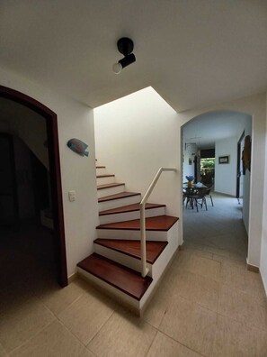 Un escalier avec des marches en bois et une rampe métallique, menant à un espace repas comprenant une table et des chaises.