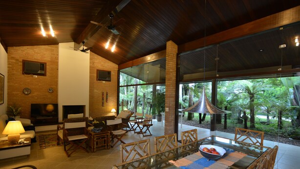 Un amplio espacio habitable con una mesa de vidrio, muebles de mimbre y vistas a exuberante vegetación.