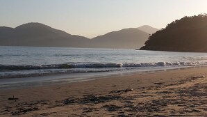Una playa con olas tranquilas, una orilla arenosa y colinas a lo lejos.