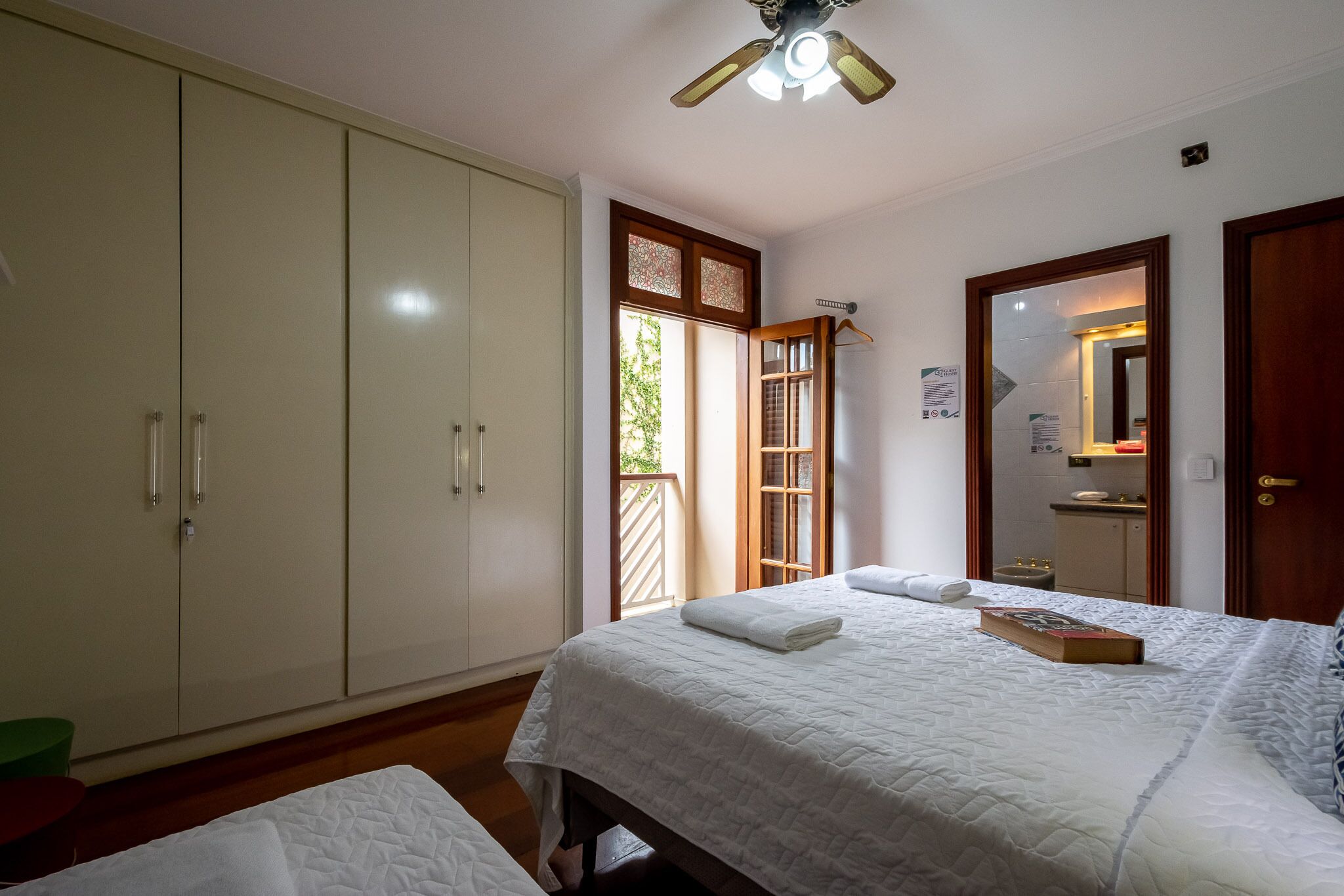Une chambre à coucher comprenant un lit, une armoire, un ventilateur de plafond et une fenêtre donnant sur un paysage verdoyant.