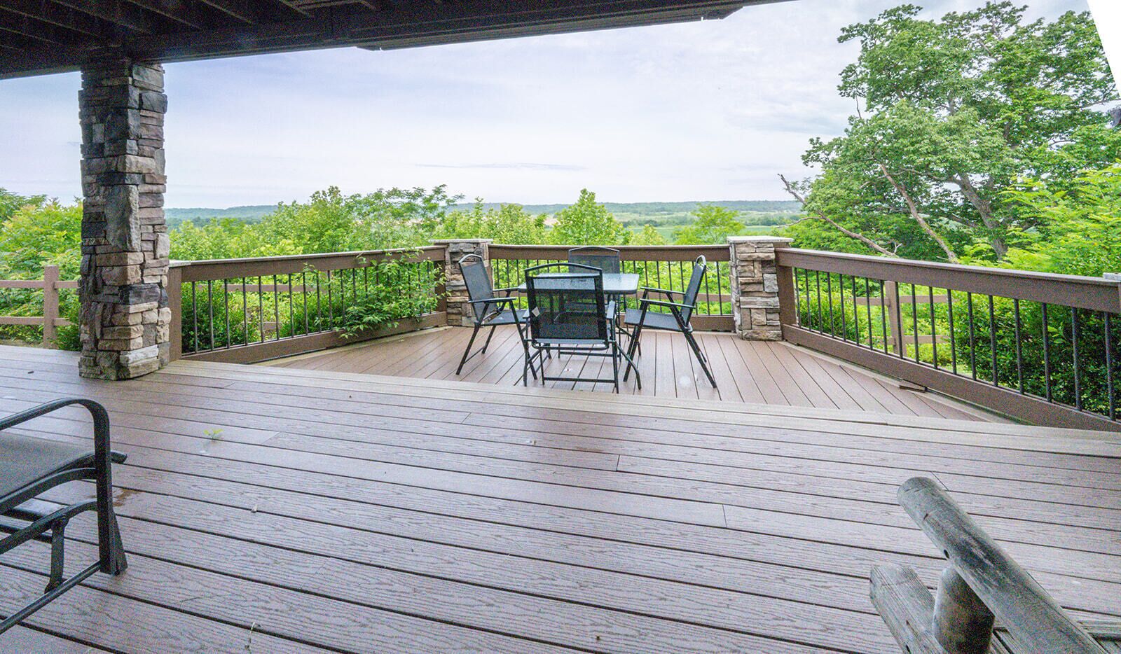 A wooden deck with stone pillars, a table, and two chairs.