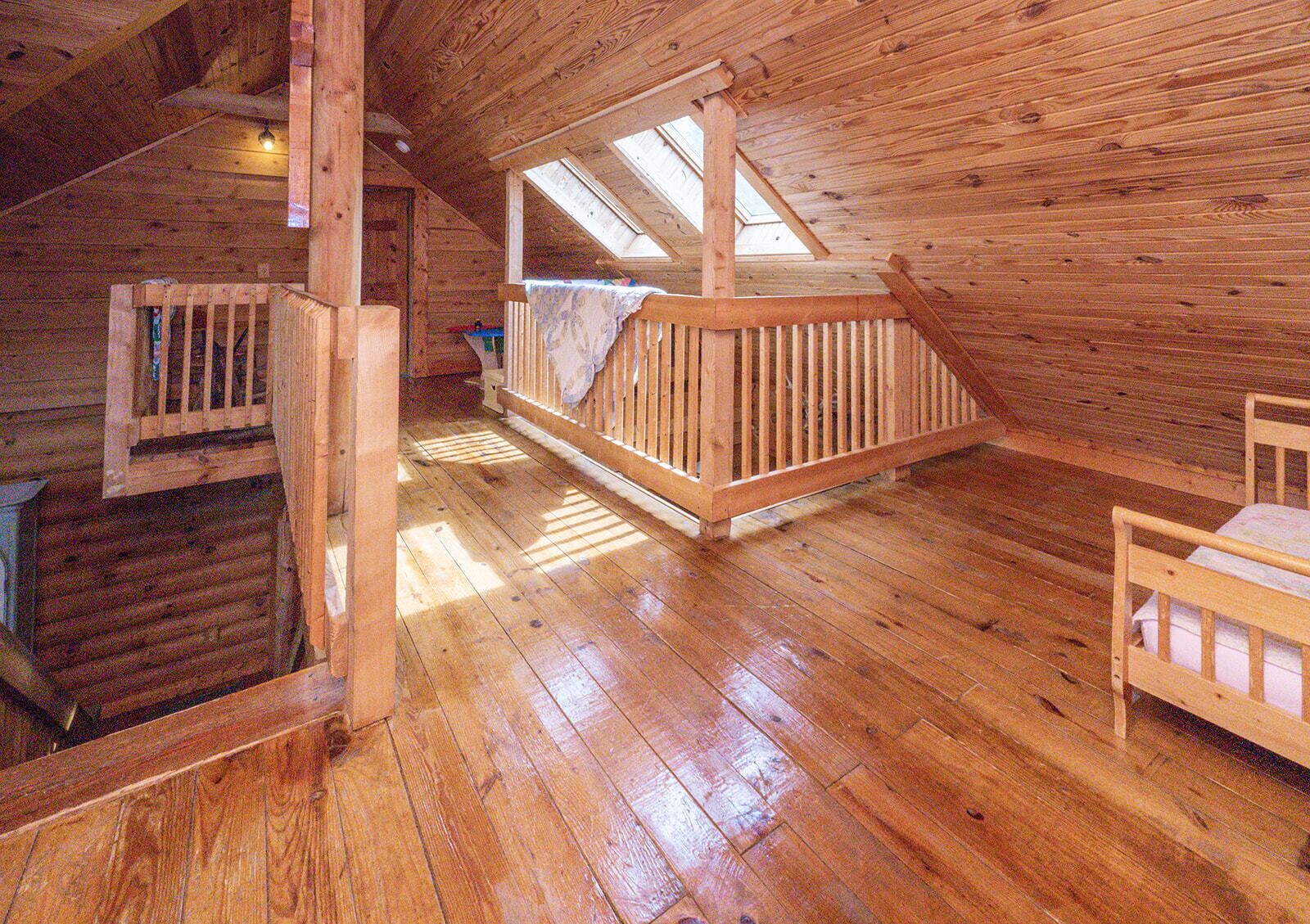 A wooden cabin with a loft bedroom, a balcony, and a small seating area.