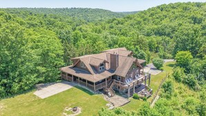 A large, two-story log cabin with a wrap-around porch, a covered deck, and a well-maintained lawn.