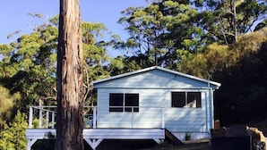 A small, single-story wooden cabin with a porch, surrounded by trees and natural landscape. - Bayview Bruny Island Beach House (Adventure Bay)