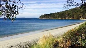 A beach with clear blue water, sandy shore, and dense green foliage. - Bayview Bruny Island Beach House (Adventure Bay)