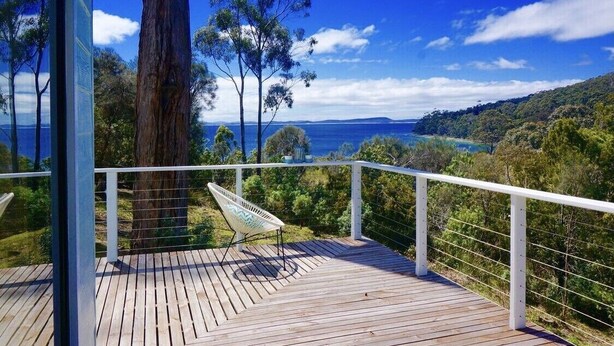 A wooden deck with a hammock, overlooking a coastal landscape with trees and a view of the sea. - Bayview Bruny Island Beach House (Adventure Bay)