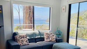 A modern living room with a large window offering a view of the sea and hills. - Bayview Bruny Island Beach House (Adventure Bay)