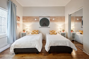 Une chambre avec deux lits, des lambris en bois sur les murs, un grand miroir et des tables de chevet avec des lampes et des plantes en pot.