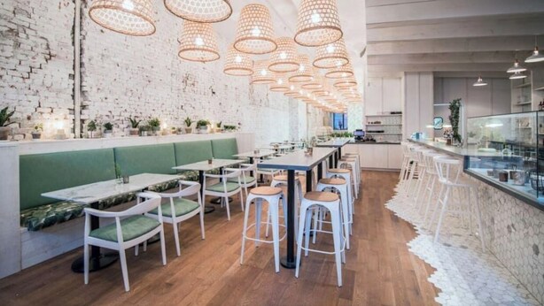A modern restaurant with a brick wall, green booths, wooden tables, and hanging pendant lights. - MTLVR #11 | Central, Group Friendly, Patio (Montreal)