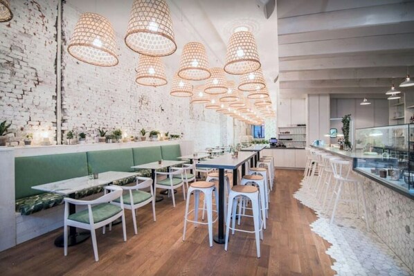 A modern restaurant with a brick wall, green booths, wooden tables, and hanging pendant lights. - MTLVR #11 | Central, Group Friendly, Patio (Montreal)