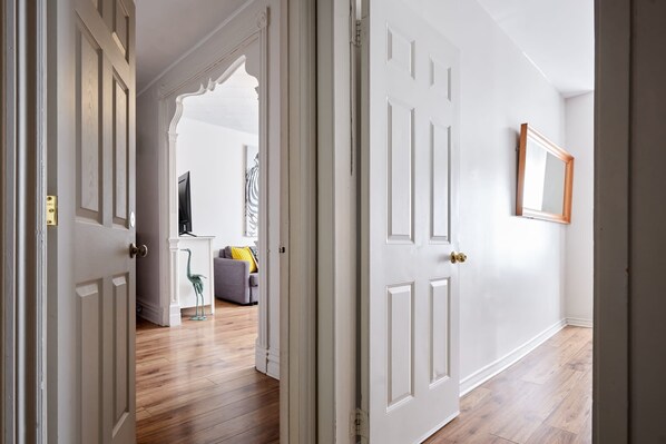 A hallway with white doors, a wooden floor, and a mirror on the wall. - MTLVR #11 | Central, Group Friendly, Patio (Montreal)