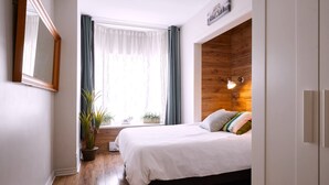 A bedroom with a bed, a window with curtains, a potted plant, and a wooden accent wall. - MTLVR #11 | Central, Group Friendly, Patio (Montreal)