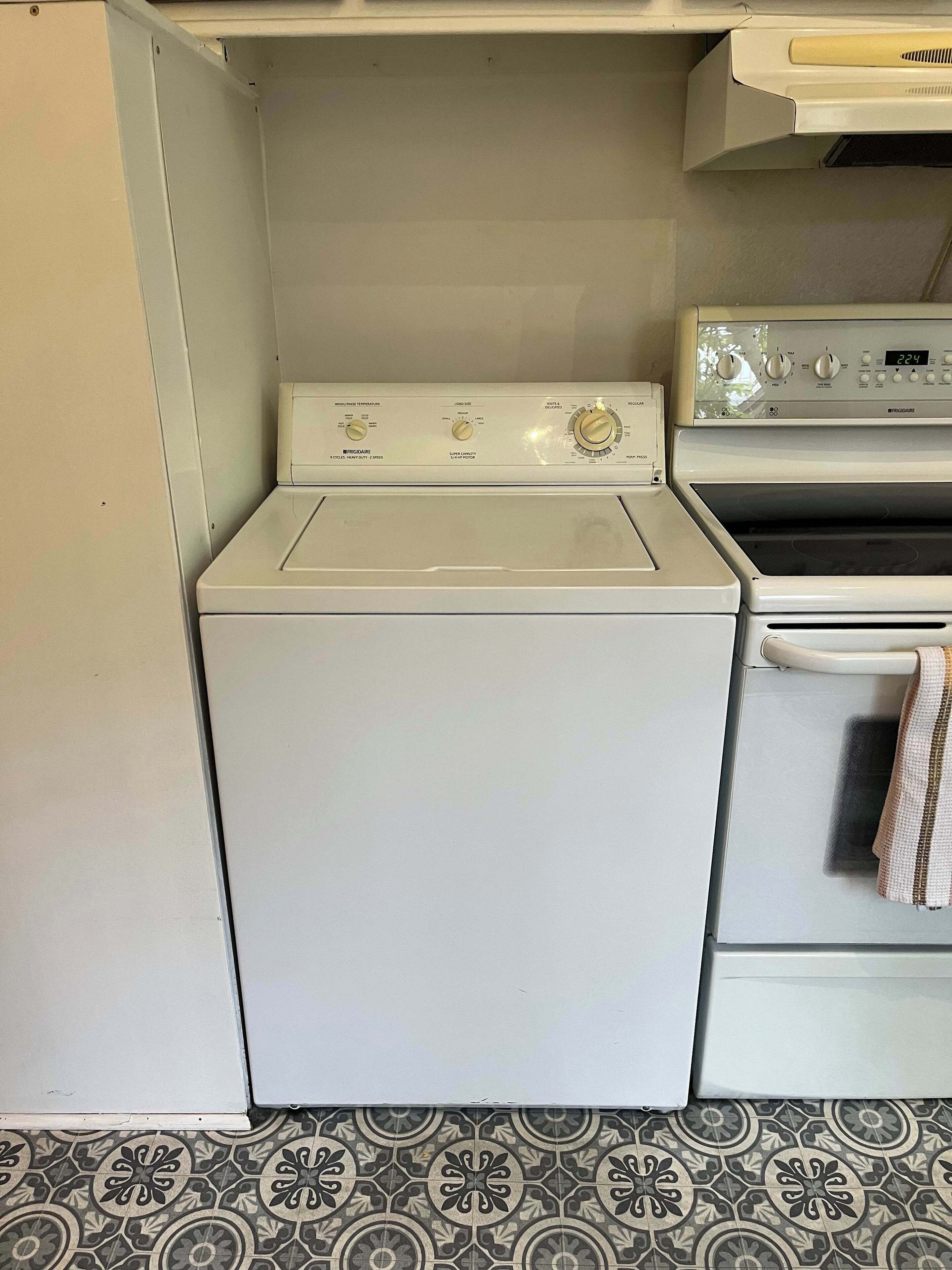 Kompakti pyykinhuone, jossa on etuaukollinen pesukone ja kuivausrumpu, pieni uuni ja kuviollinen lattialaatoitus.