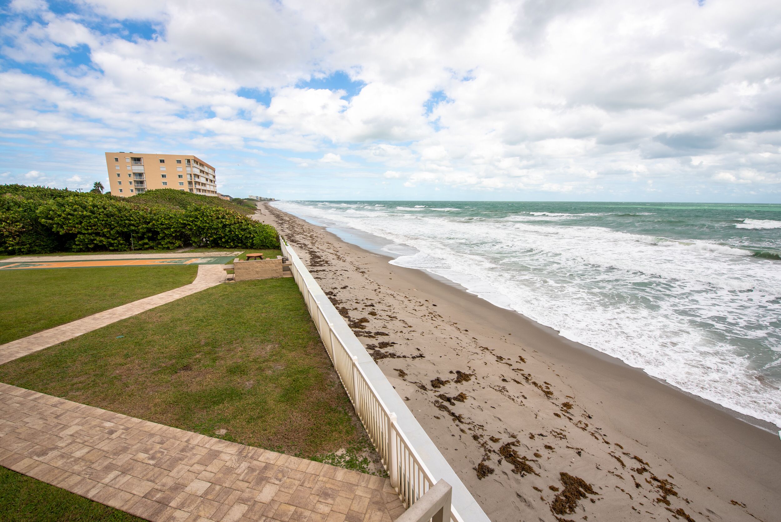 A beach with a pathway leading to a building, a grassy area, and the ocean.