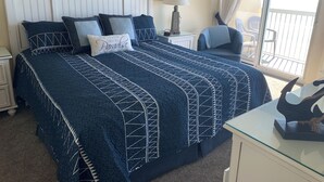 A bedroom with a large bed, a nightstand, a chair, a lamp, and a view of the balcony.