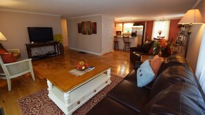 Una sala de estar con una mesa de centro de madera, un sofá de cuero, un televisor y una cocina al fondo.