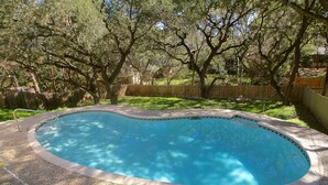 Una piscina amb vora de rajola, envoltada per una tanca de fusta i arbres.