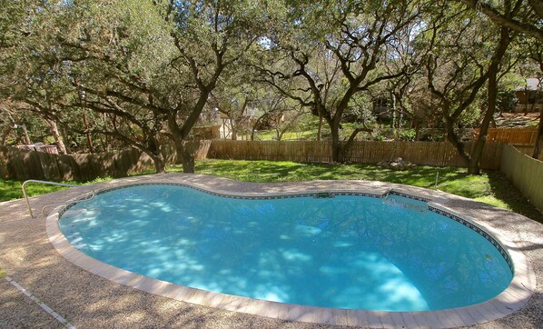 A swimming pool with a tiled edge, surrounded by a wooden fence and trees.