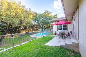 A backyard with a swimming pool, a patio with outdoor furniture, and a fenced area with trees.