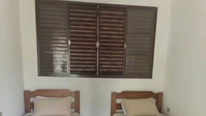 Twee eenpersoonsbedden met houten frames en beige beddengoed, een raam met horizontale zonwering en een betegelde vloer.