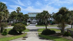 A residential street with a two-story house, palm trees, and a clear sky. - A traditional beach house located near historic downtown Charleston (Isle of Palms)