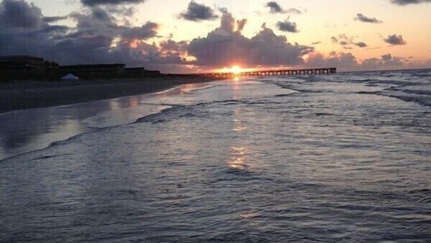 A beach scene with a pier extending into the water during sunset. - A traditional beach house located near historic downtown Charleston (Isle of Palms)