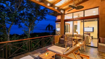 Un vaste balcon doté de mobilier en bois, d’un coin repas et offrant une vue sur l’océan au crépuscule.