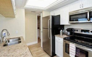 Eine Küche mit einem Edelstahl-Kühlschrank, einer Mikrowelle und einem Ofen, einer Granit Arbeitsplatte und weißen Schränken.