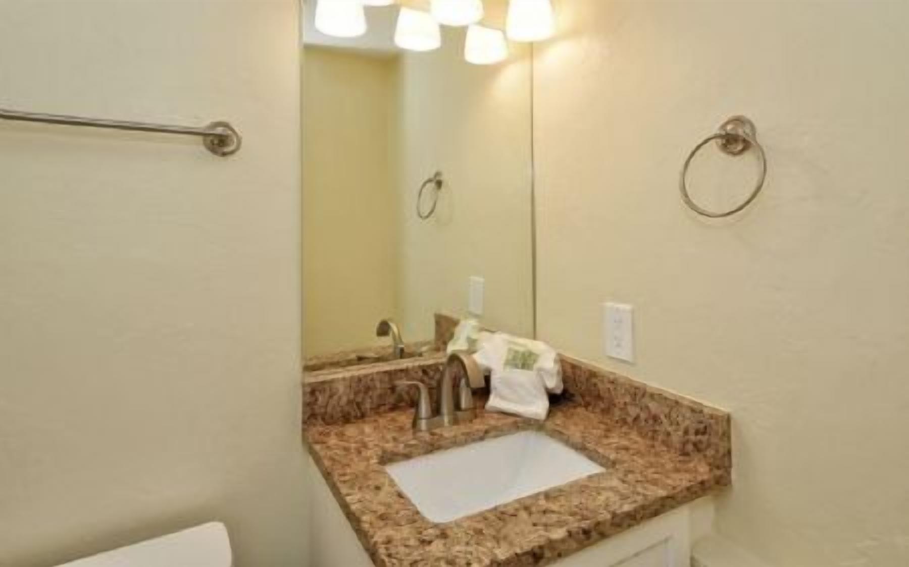 A bathroom with a granite countertop sink, a towel rack, and a mirror.