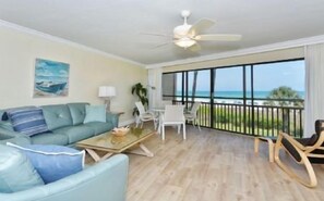 Ein geräumiges Wohnzimmer mit großem Fenster, Deckenventilator, Sofa, Couchtisch und Meerblick.